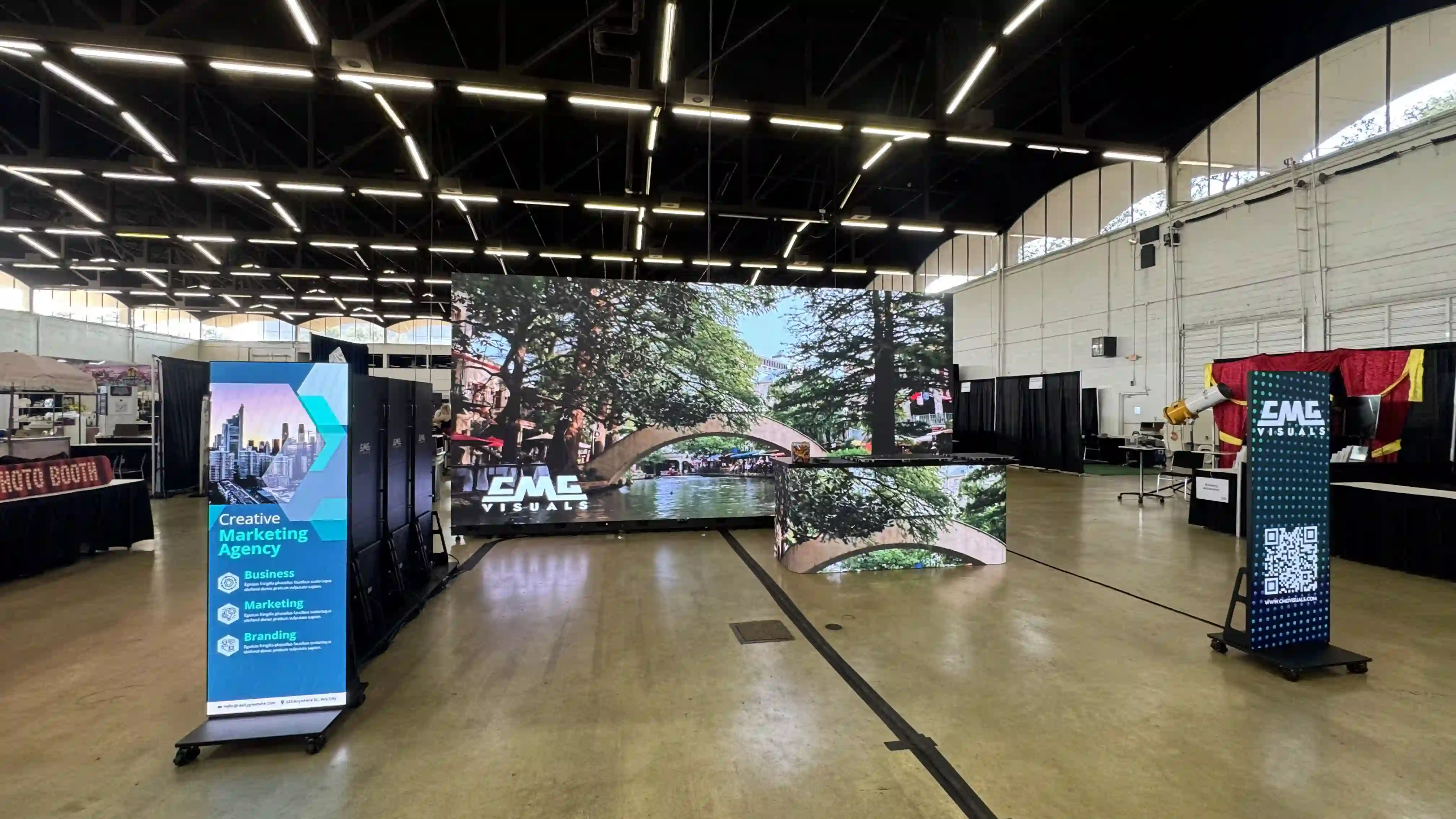 LED video wall rental display by CMG Visuals at a trade show, featuring a large 4K indoor screen, LED DJ booth, and digital signage pillars showcasing marketing content and QR codes.