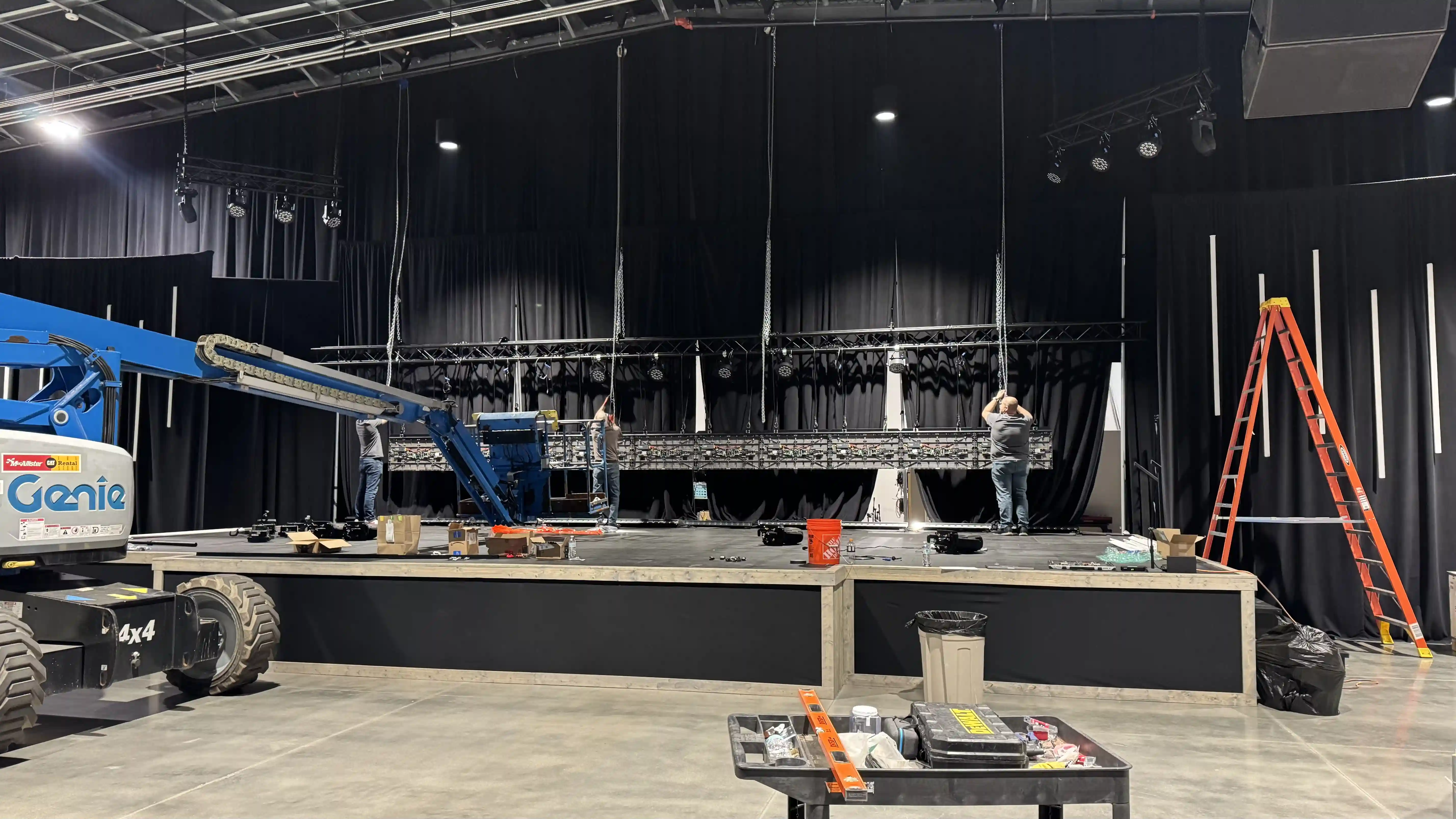 Technicians working to assemble and rig the center LED wall at The Rock Church in Fenton, MI, with panels being installed and lifts positioned on stage.