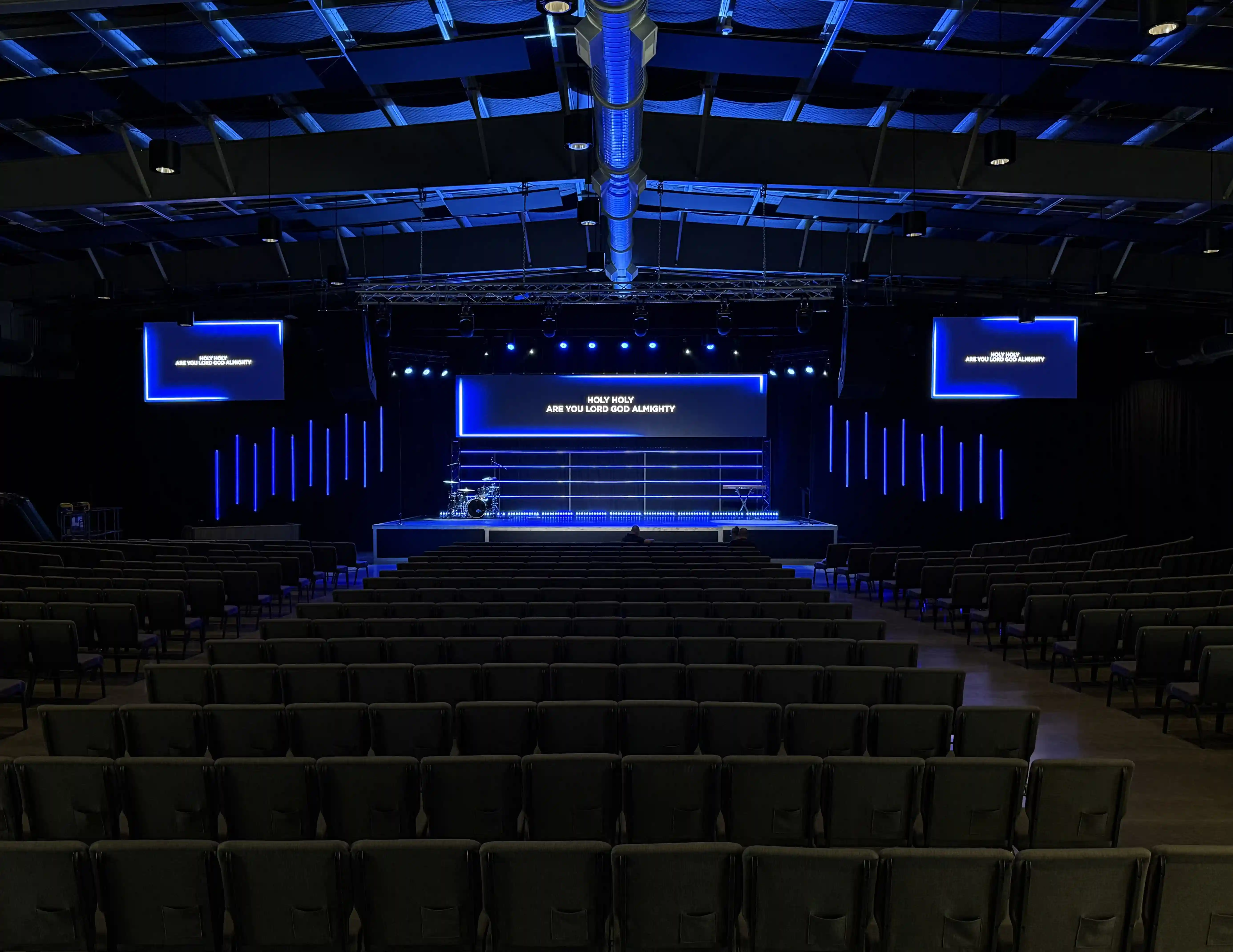 Wide view of The Rock Church auditorium in Fenton, MI, showing the newly installed three-screen LED setup with the large center display illuminated during a worship environment.