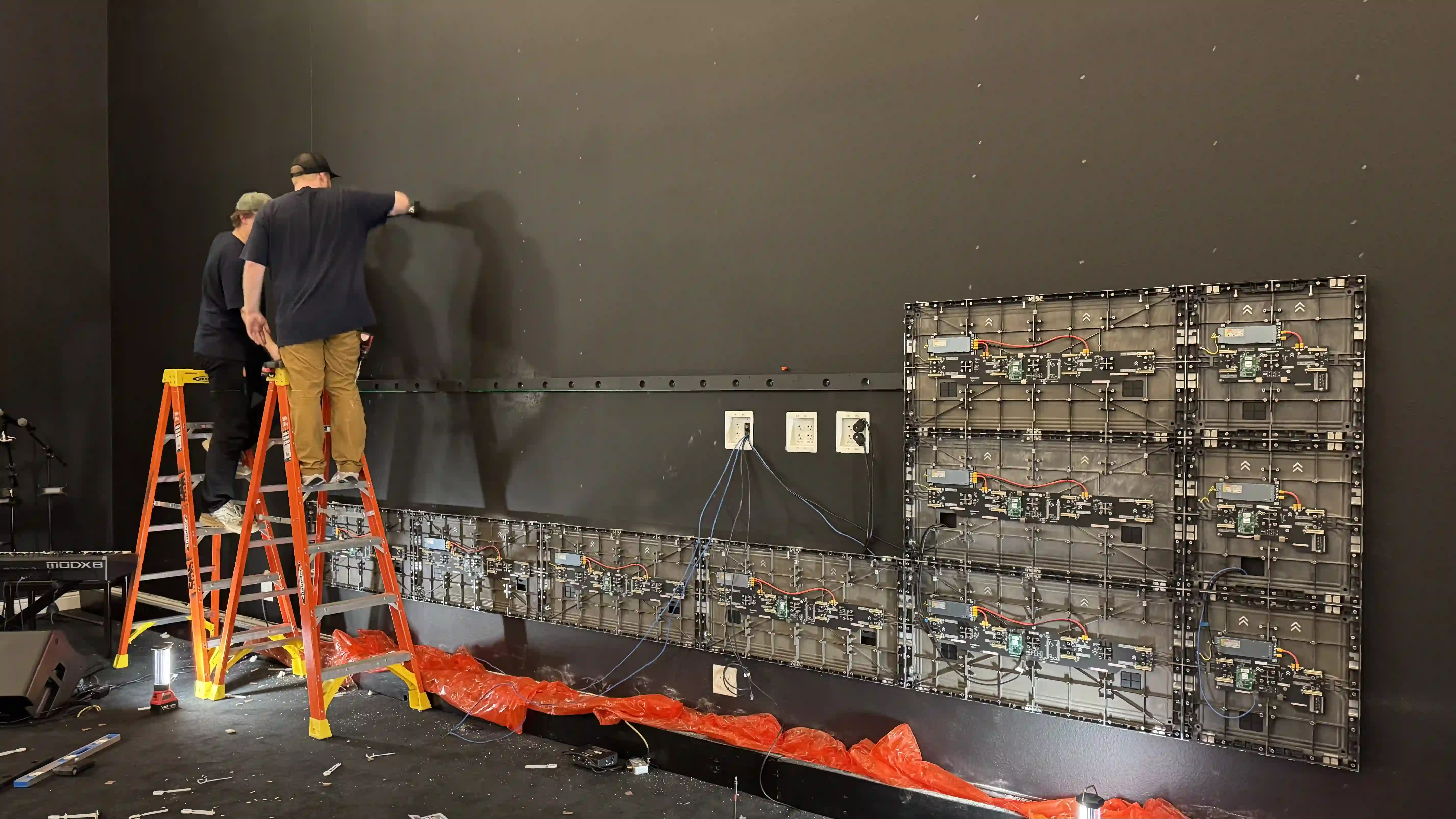 During install: technicians on ladders mounting first LED cabinets and cabling on sanctuary wall at Keystone Church Mesquite, Texas.