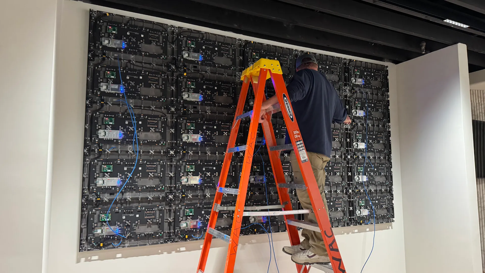 Technician on ladder installing LED video wall panels indoors