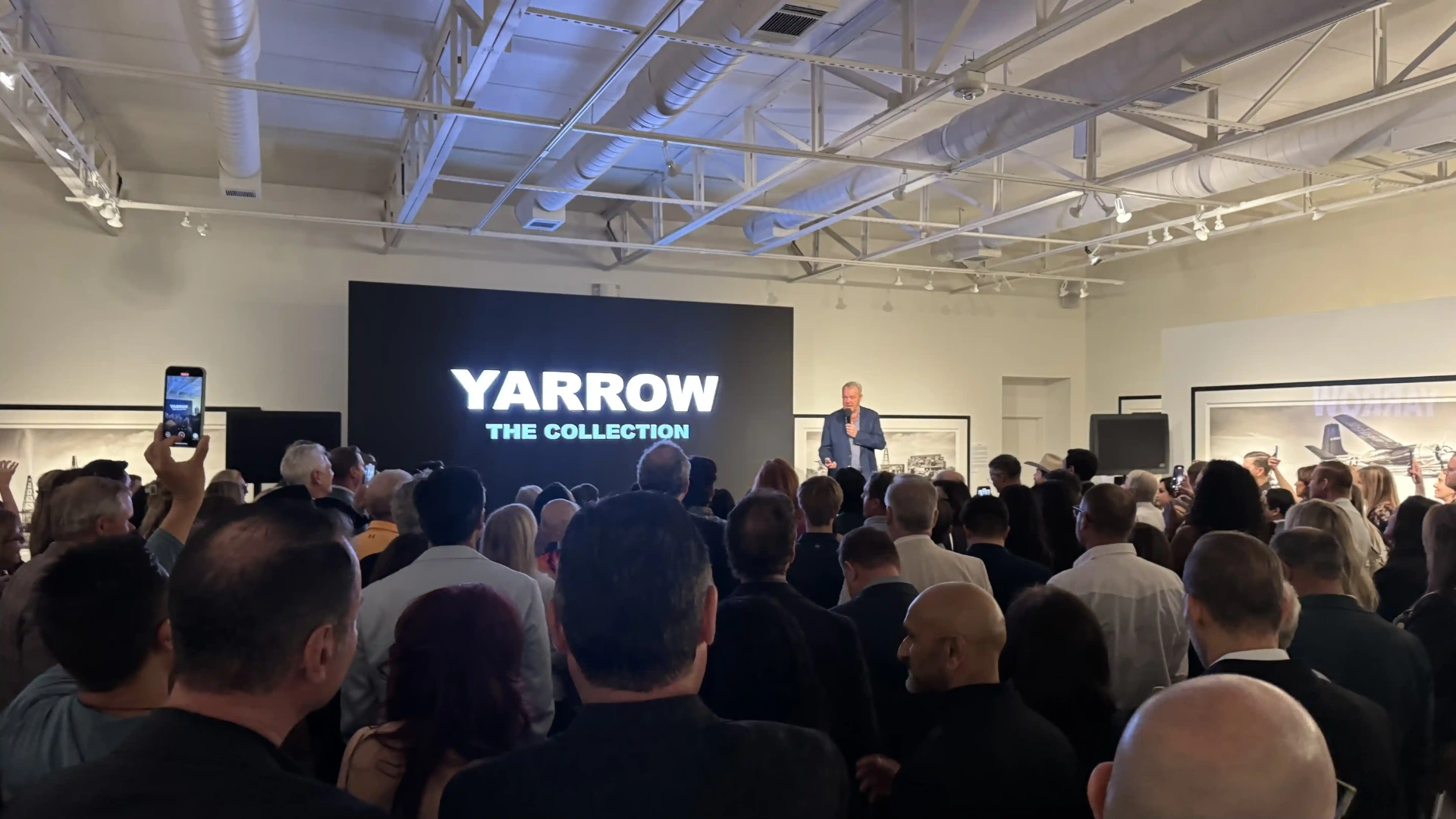 Speaker presenting in front of LED video wall at gallery event.