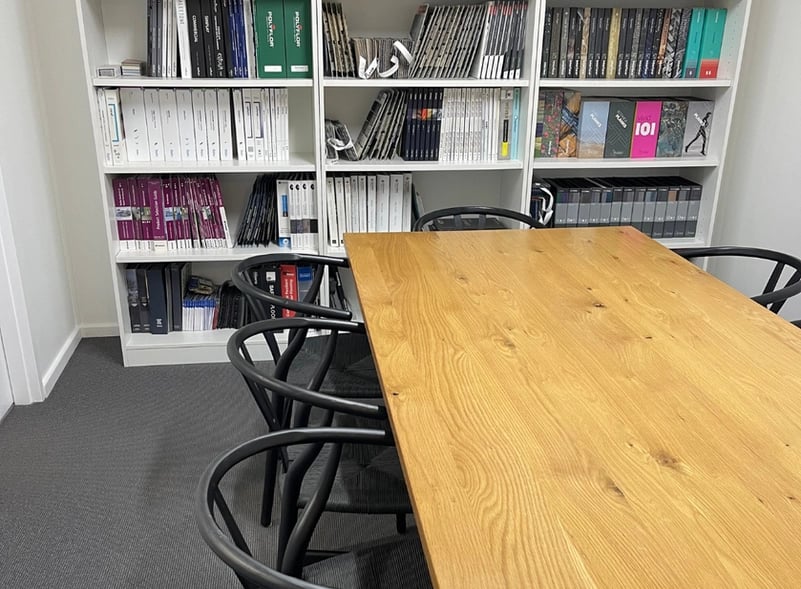 Office meeting area with a wooden table, black chairs, and shelves filled with binders and books