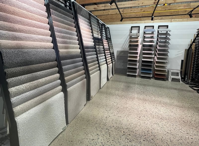 Carpet and flooring sample displays in a showroom with polished concrete floors and wooden ceiling beams