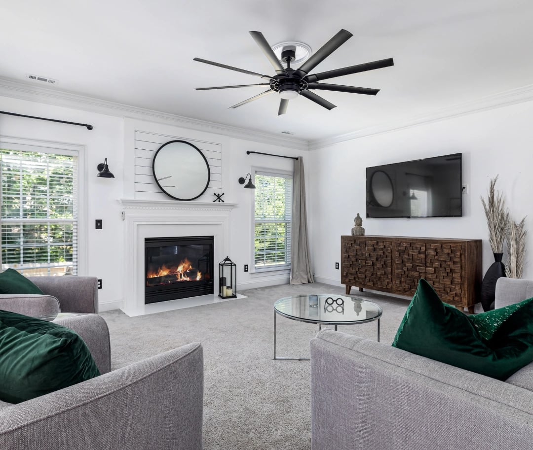 Modern living room with a fireplace, large ceiling fan, gray furniture, and green accent pillows