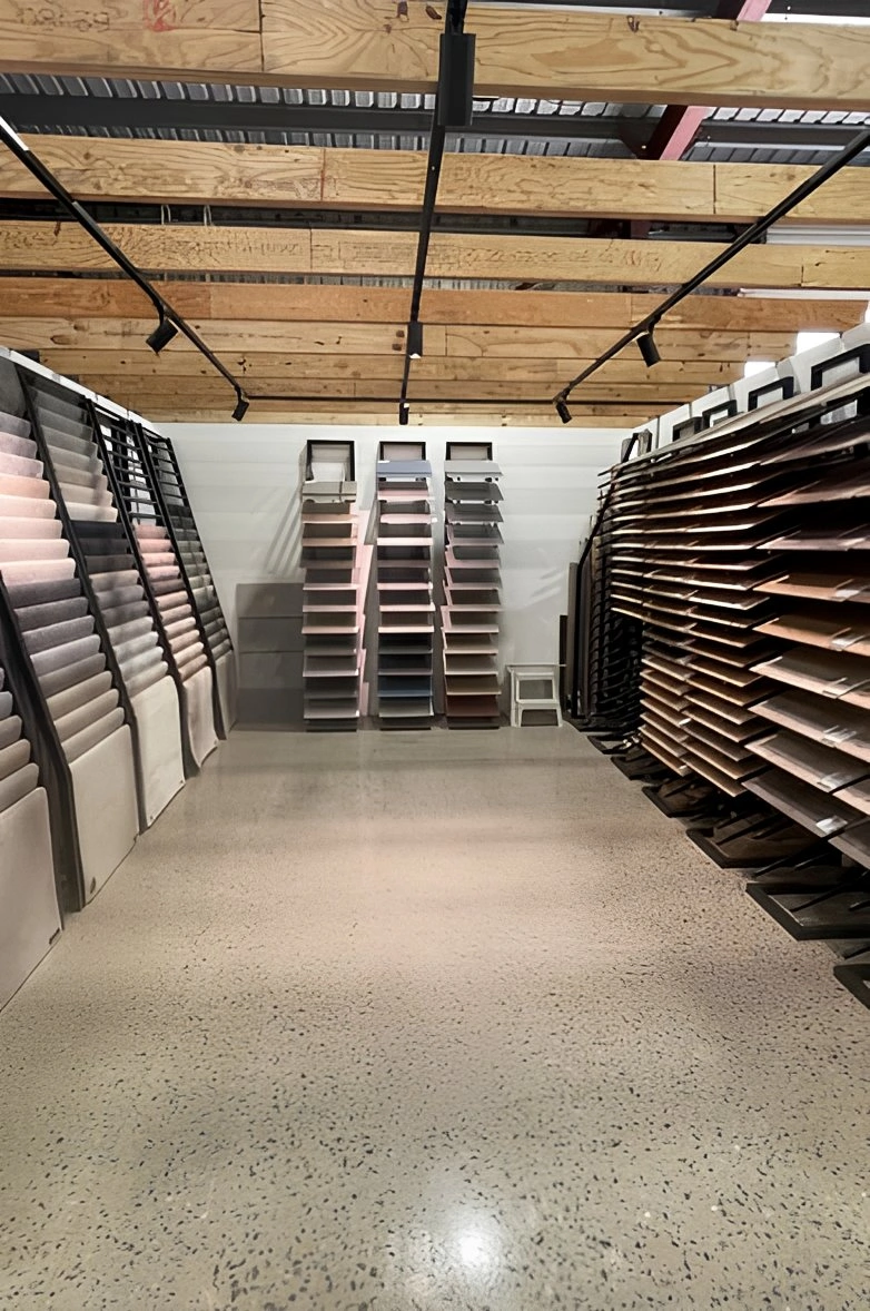Flooring showroom with carpet and wood sample displays under exposed wooden ceiling