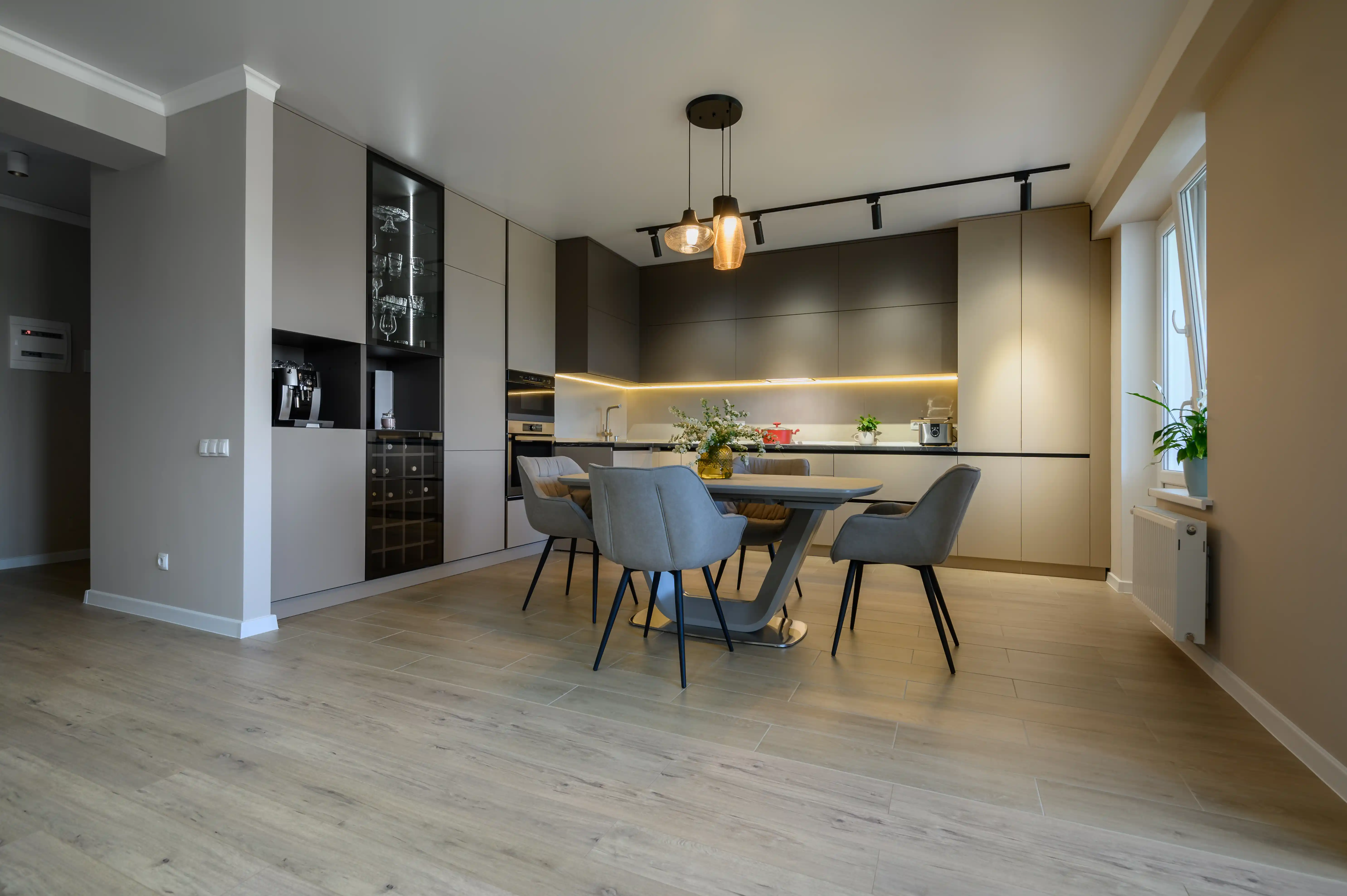 Modern kitchen and dining area with beige and dark cabinetry, light wood flooring, and pendant lighting