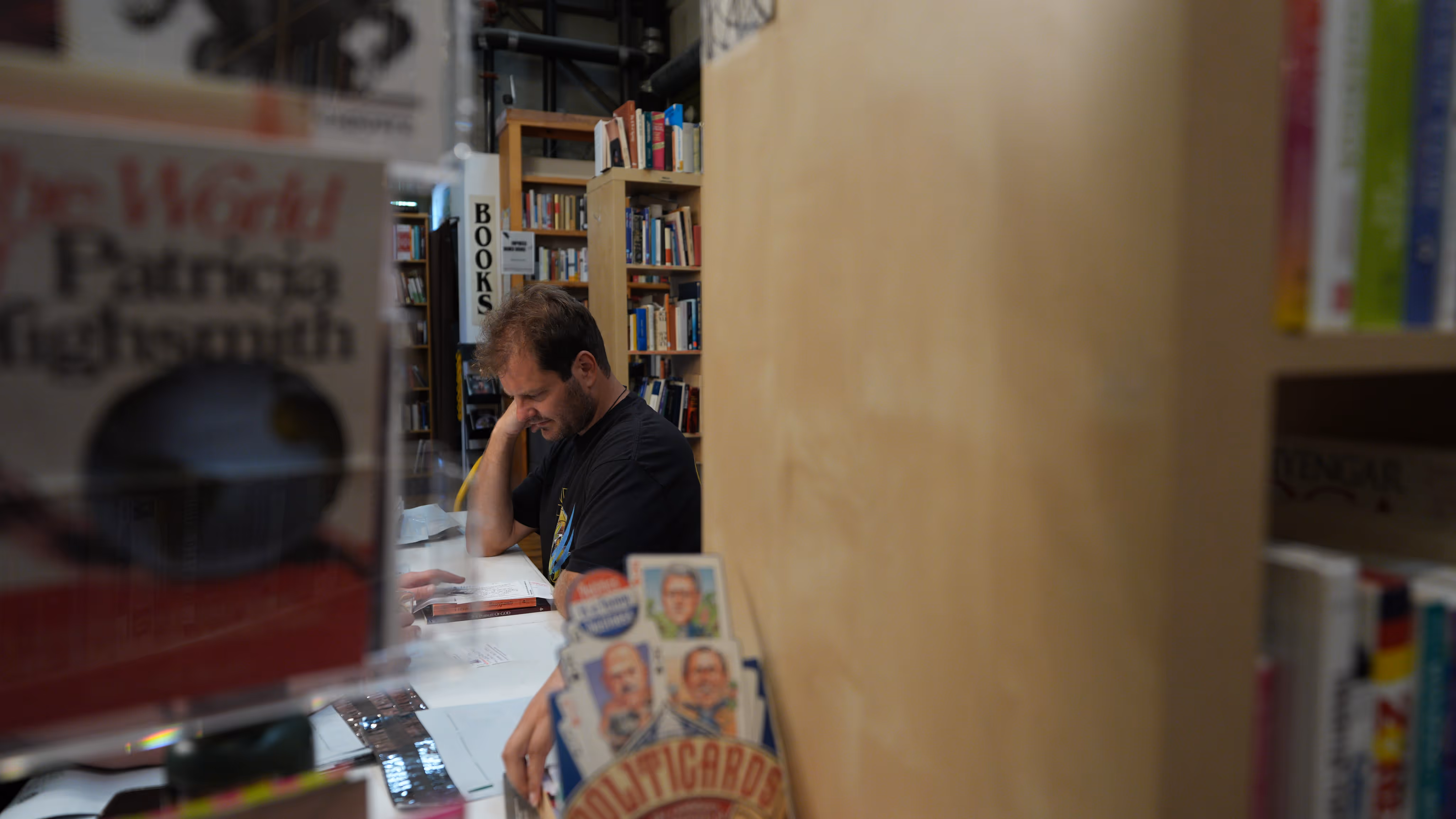 A man reading a book at a table in a bookstore surrounded by shelves filled with books.