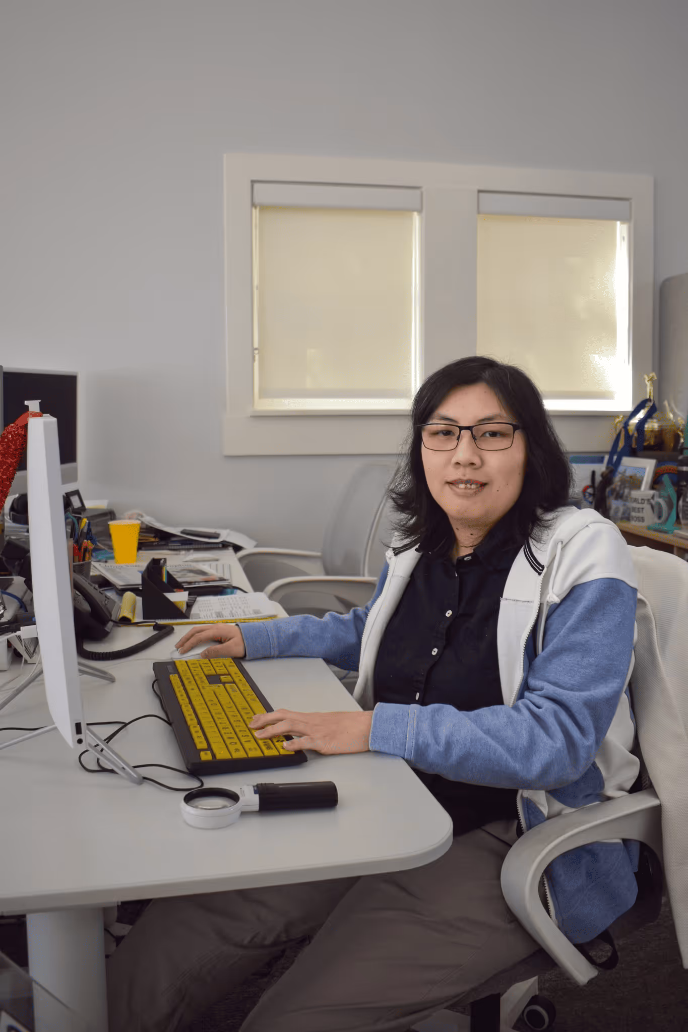 Person with glasses sitting at a desk using a computer with a yellow-marked keyboard.