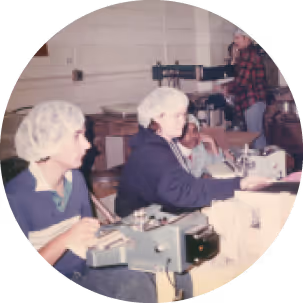 Three factory workers wearing hairnets operate packaging machines in an industrial setting.