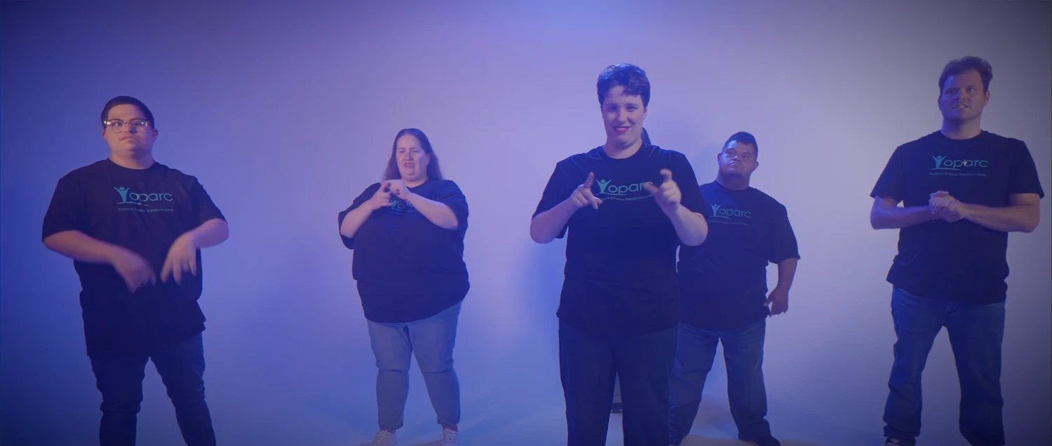 Five people wearing black Oparc t-shirts standing in a row participating in sign language.