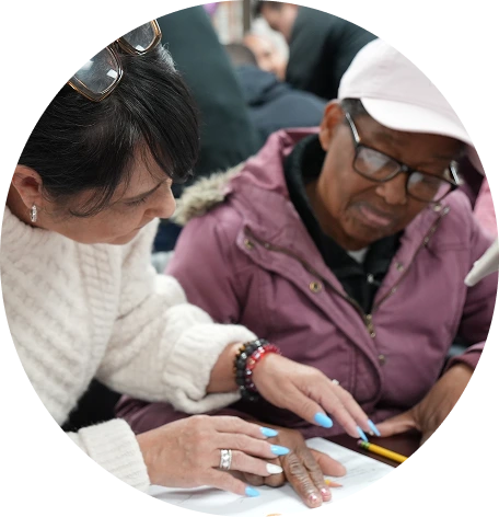 Two women closely collaborating and reviewing a document together, one wearing glasses and a white sweater, the other in a purple jacket and white cap.