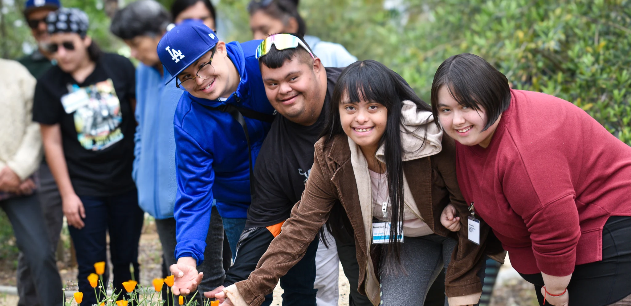 Group of smiling young adults outdoors reaching toward orange flowers.