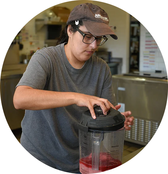 Person wearing glasses and a cap operates a blender with red ingredients in a kitchen setting.