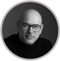 Portrait en noir et blanc d'un homme portant des lunettes et un col roulé, souriant légèrement.