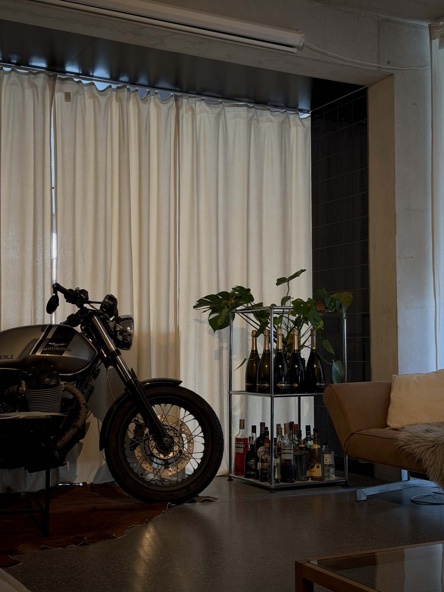 A stylish interior featuring a vintage motorcycle next to a modern shelving unit with various bottles and plants. Light-colored curtains frame the space, contributing to a contemporary atmosphere suitable for a Performance Marketing Agency in Zurich.