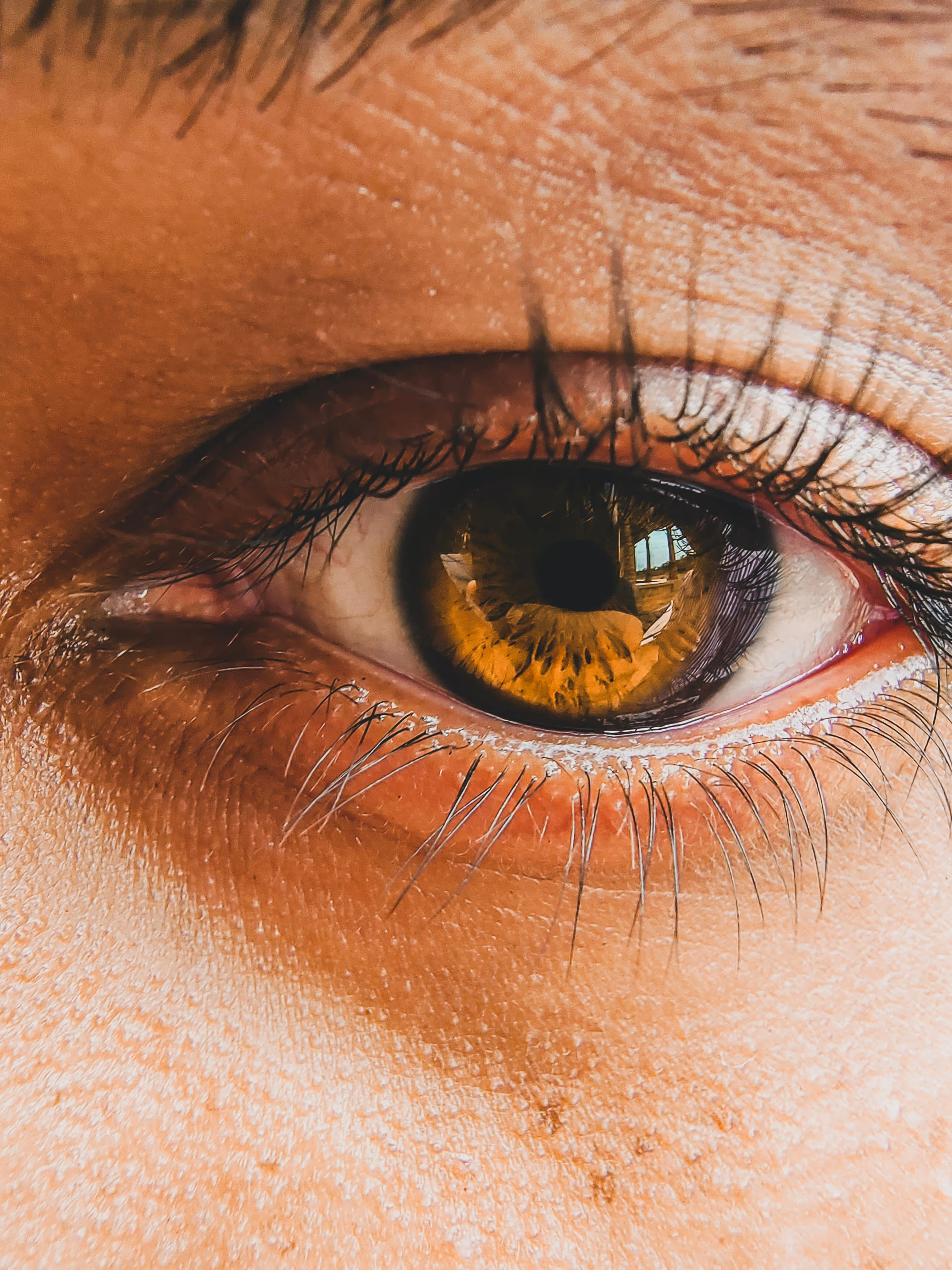 Close-up of a human eye with a brown iris and long eyelashes, highlighting details of the iris texture and the pupil.