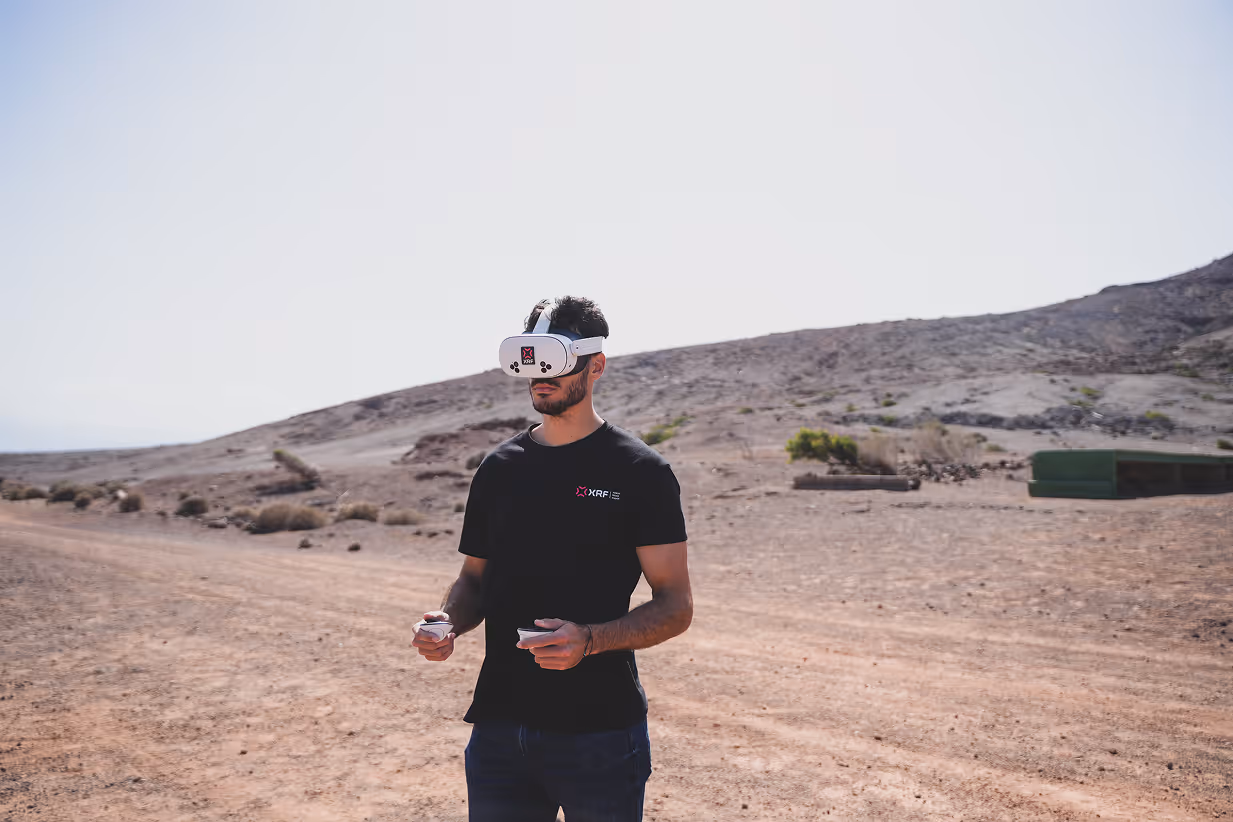 Man wearing XRF VR goggles and holding drone controllers outdoors.