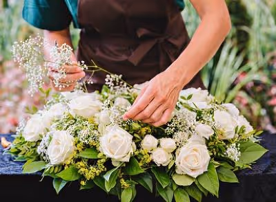 Zoom sur mains d'une femme avec un tablier qui prépare un bouquet plat de fleurs blanches