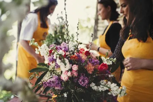 Trois femmes avec de jolis tabliers jaunes-moutardes, confectionnent des bouquets de fleurs dans un atelier