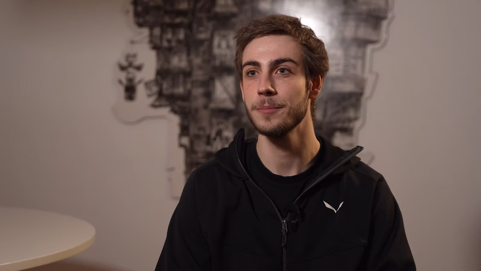 Junger Mann sitzt entspannt in einem hellen Schlafzimmer, blickt zufrieden aus dem Fenster – Symbol für besseren Schlaf durch Cannabistherapie.