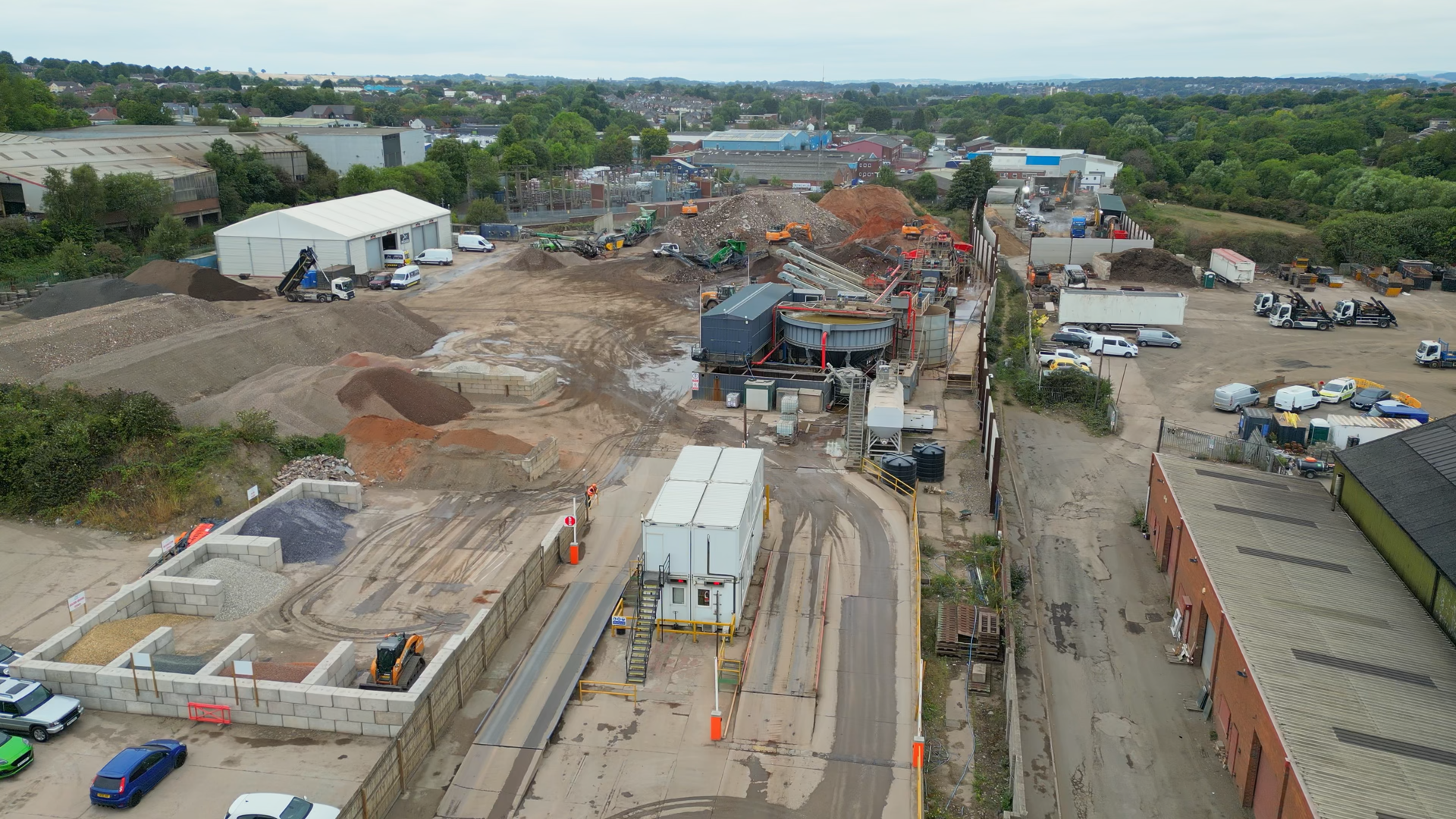 Aerial view of a construction site with piles of gravel and sand, construction machinery, and several parked vehicles.