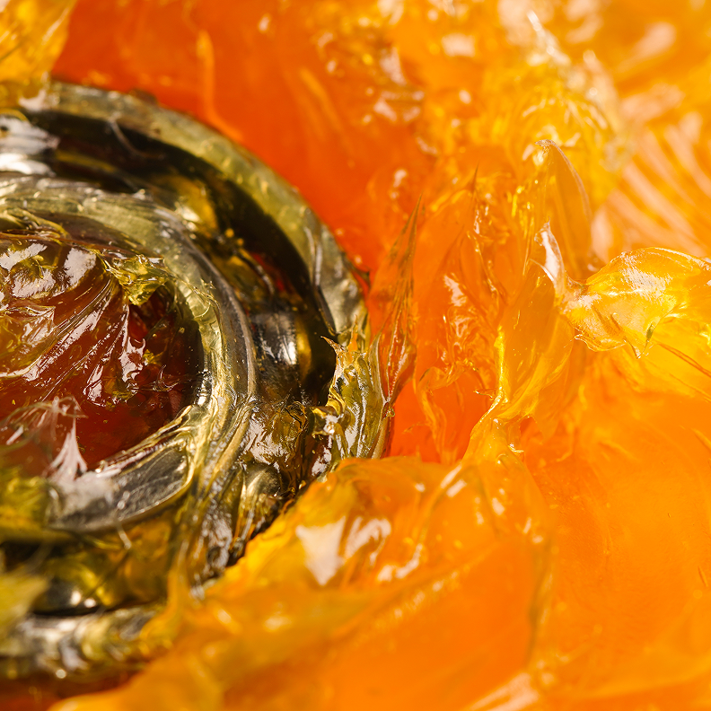 Zähflüssiger, bernsteinfarbener Schmierstoff mit metallischem Bauteil inmitten der Masse.