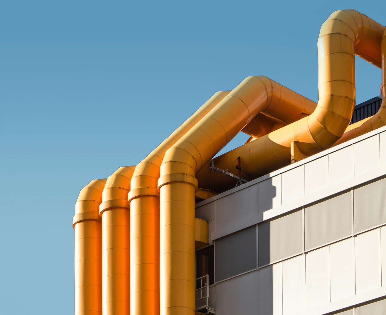 Ein modernes Industriegebäude mit auffälligen orangen Rohrleitungen, die sich über die Fassade ziehen.