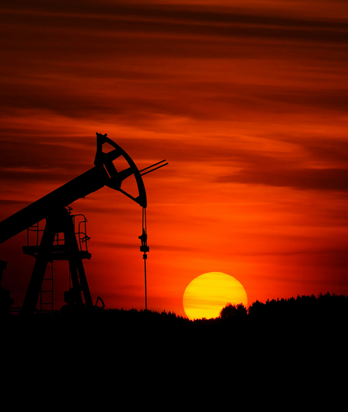 Eine Ölförderanlage steht auf einem Feld, silhouettenhaft vor einem orange-roten Abendhimmel.