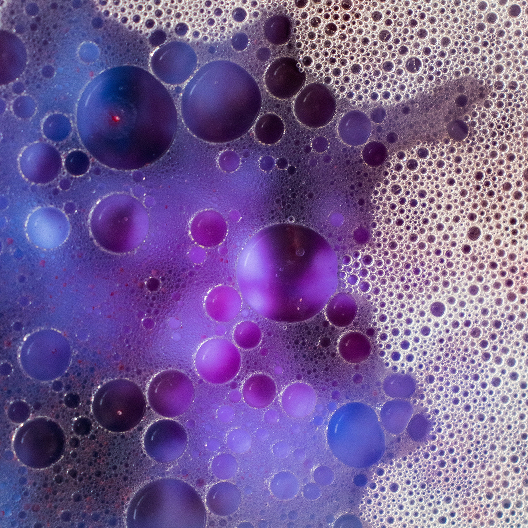 Nahaufnahme von violett-bläulichen Schaumblasen, die die Wirkung von Tensiden visualisieren.