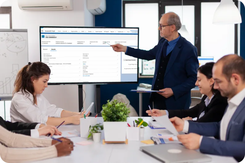 Business presentation with a large screen displaying StrataVAR’s Partner Quoting Workspace (PqW), highlighting sales order details to a team in a conference room

