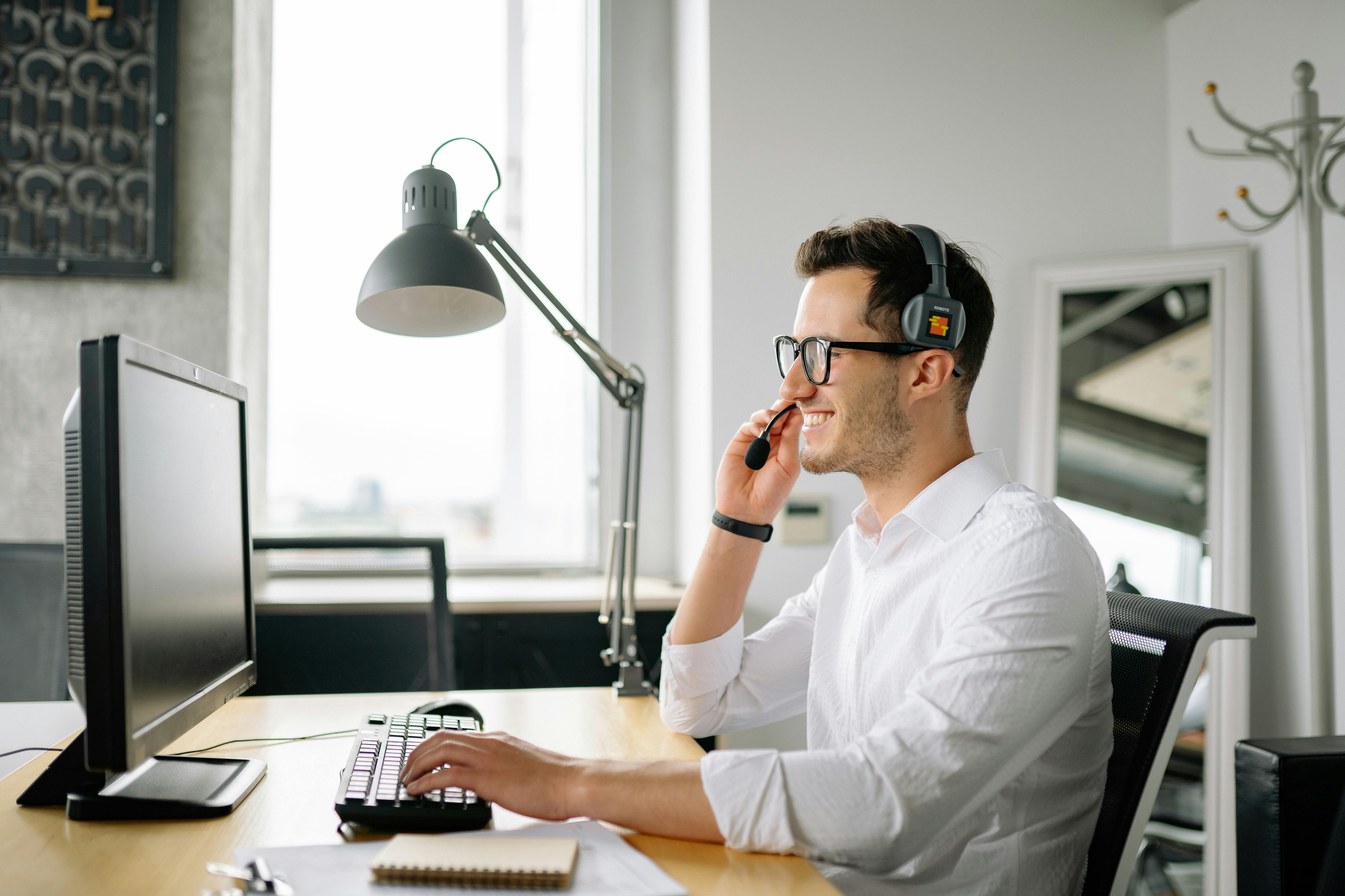 Smiling man sitting by computer desk with headset.