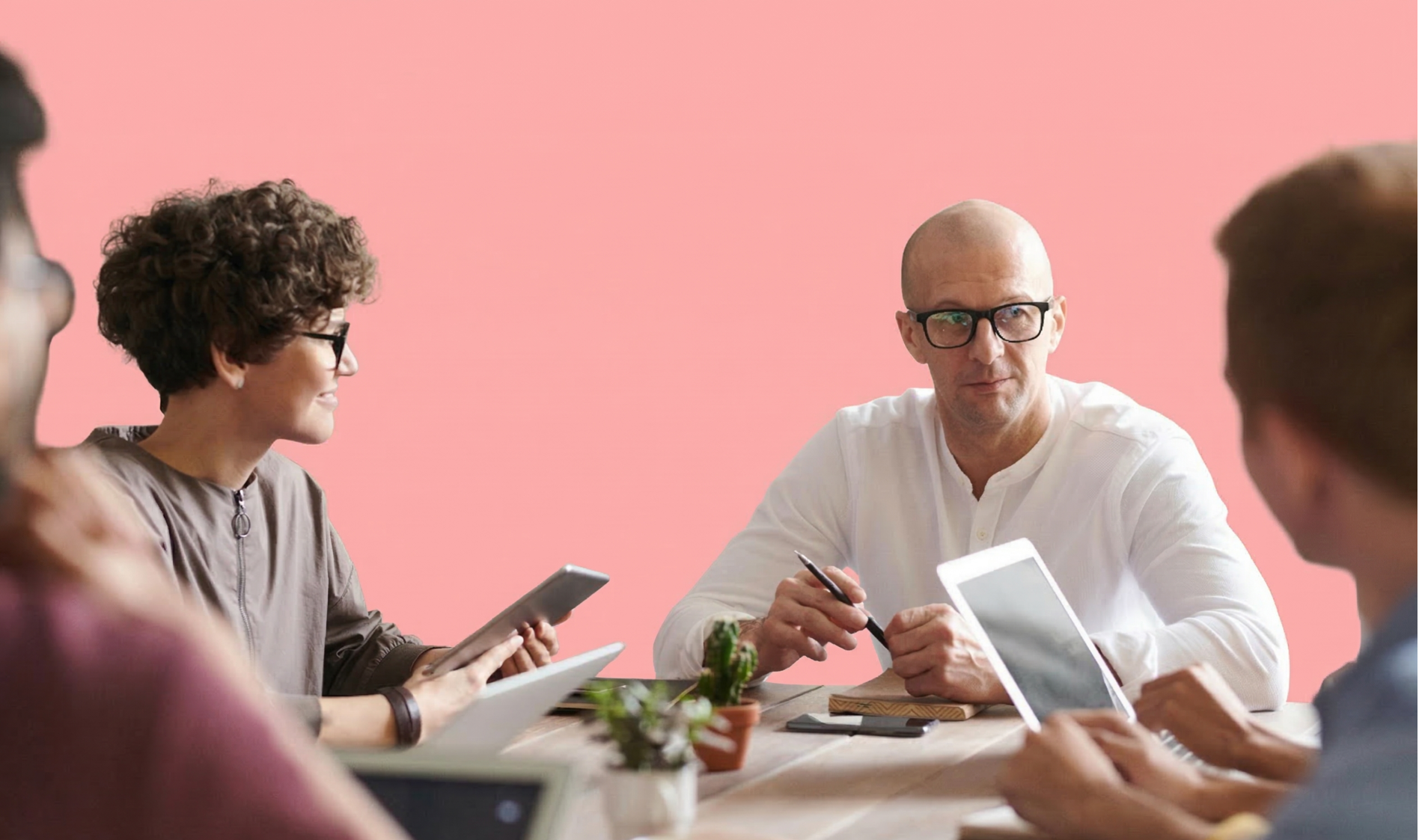People in a meeting gathered around a table using tablets and taking notes, set against a pink backdrop with the word "Work."