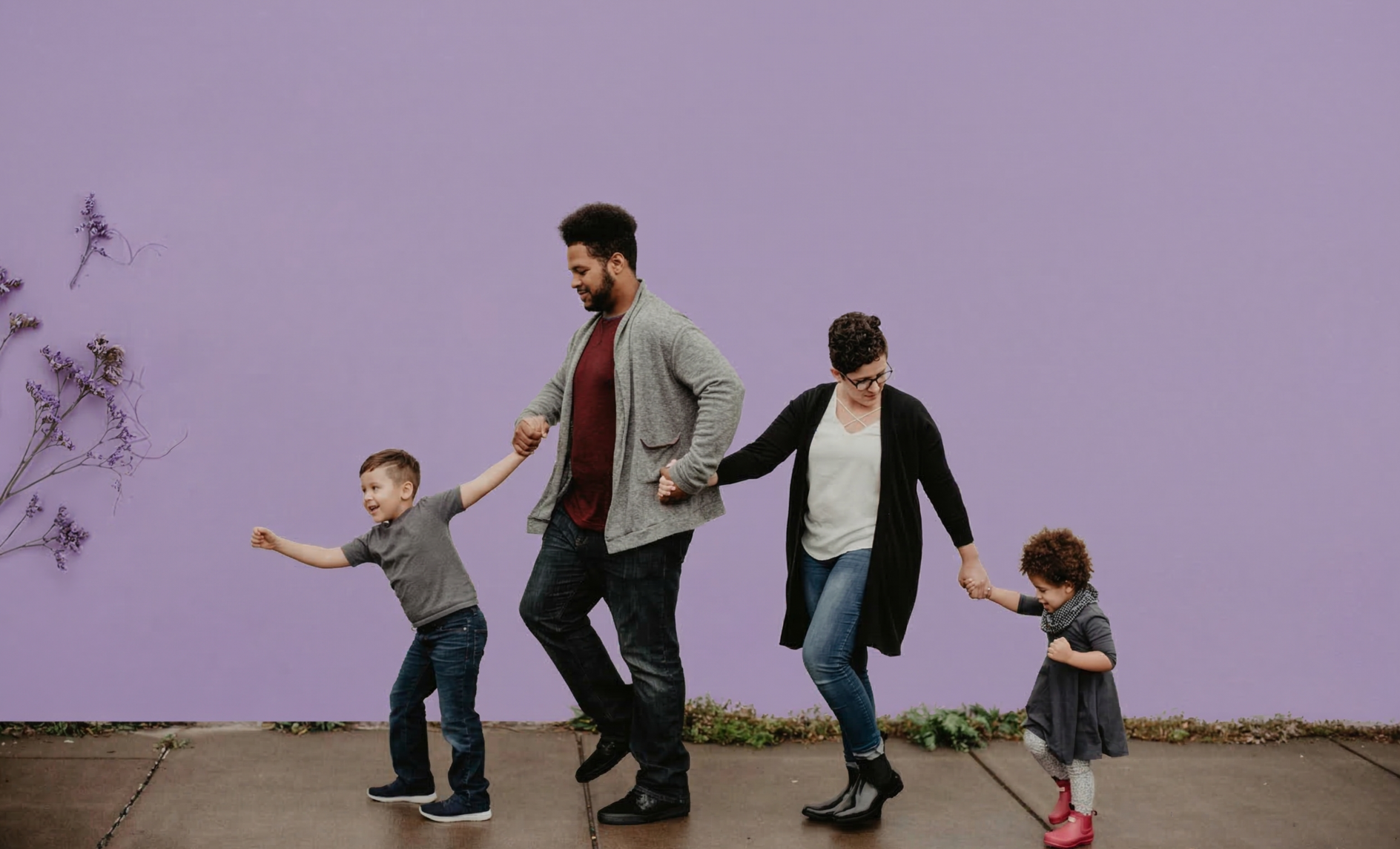 Two adults holding hands with two children as they walk along a sidewalk in front of a lavender wall labelled "Family."