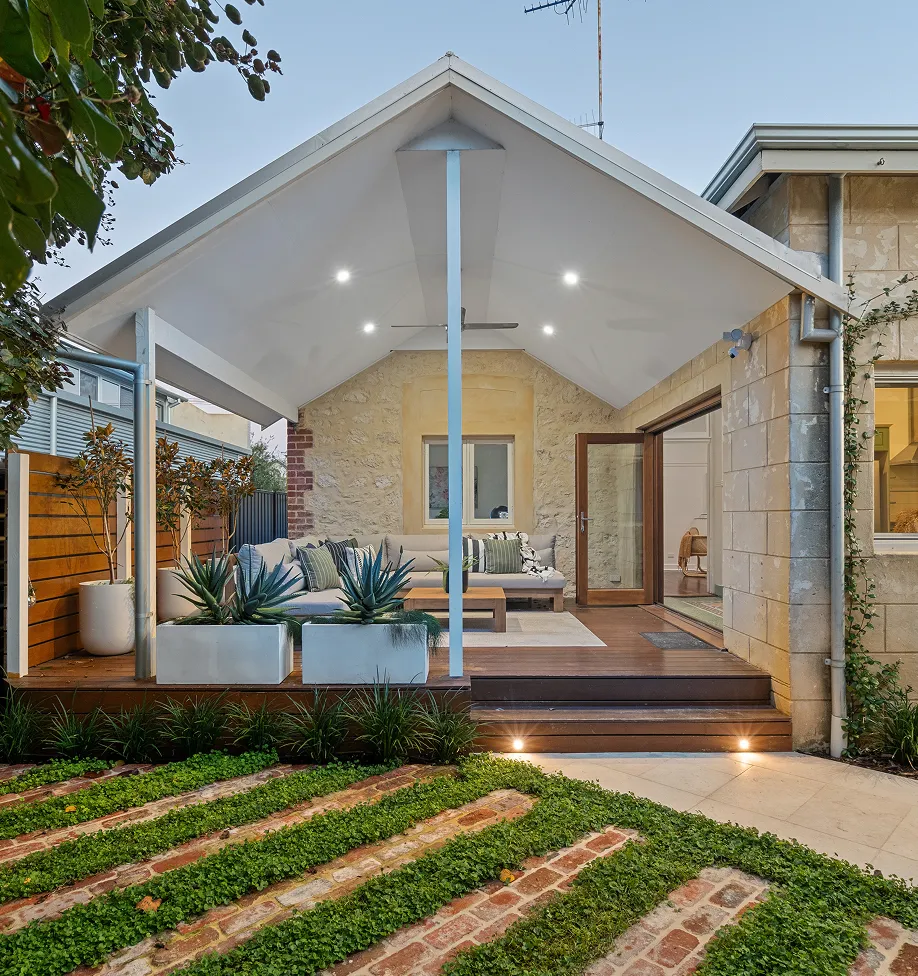 Modern covered patio with wooden deck, outdoor sofa, and decorative plants in large white planters.