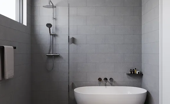 Modern bathroom with a freestanding white bathtub, wall-mounted faucet, glass shower enclosure, and gray tiled walls.