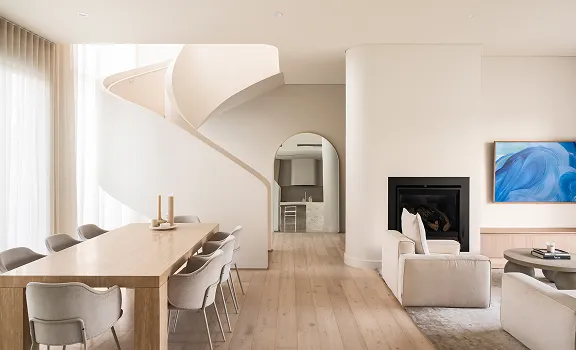 Modern open living space with a wooden dining table, gray chairs, a white spiral staircase, and a seating area with a fireplace and abstract art.