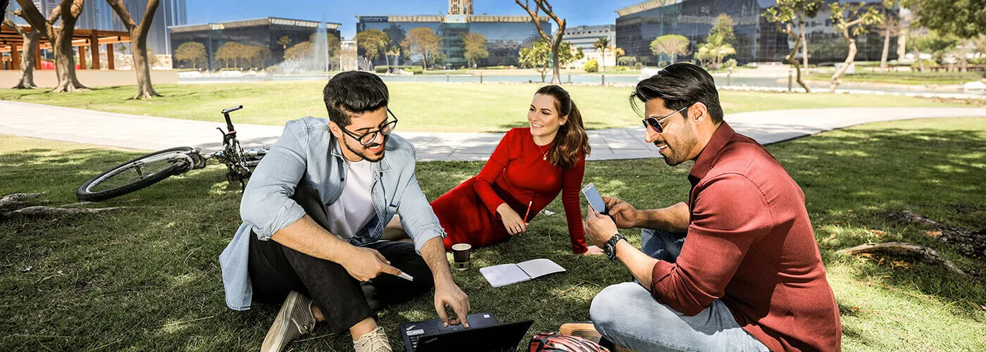 few people sitting in a park under a tree and discussing something over the laptop.