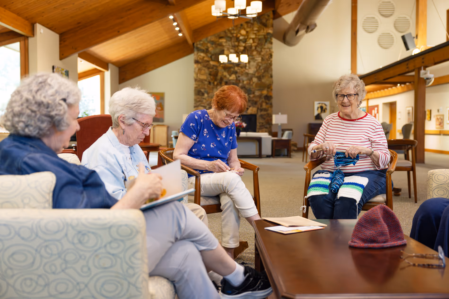 Four elderly women sitting in a community room knitting and chatting together.