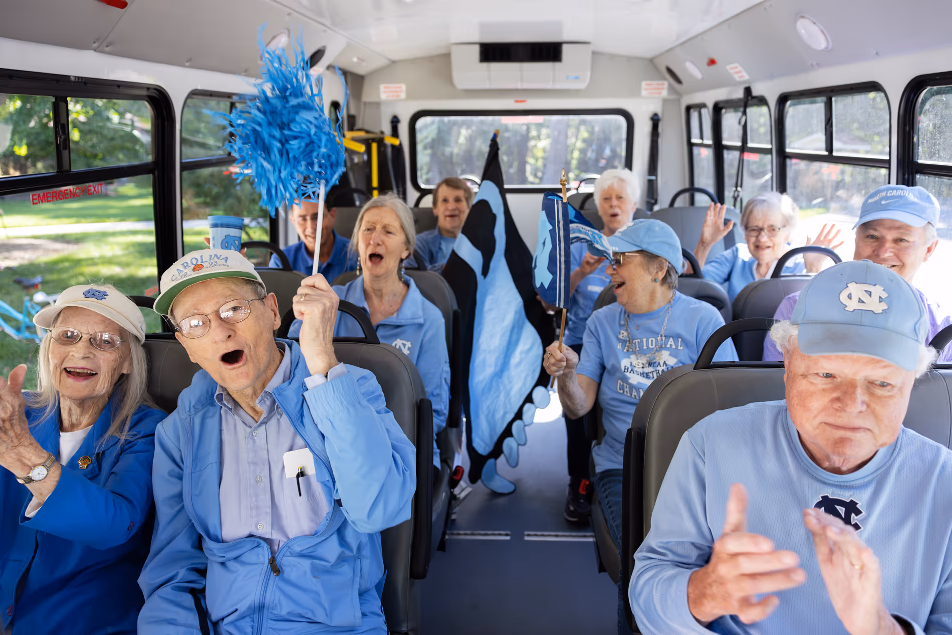 A group of elderly people in blue clothing cheer enthusiastically on a bus.