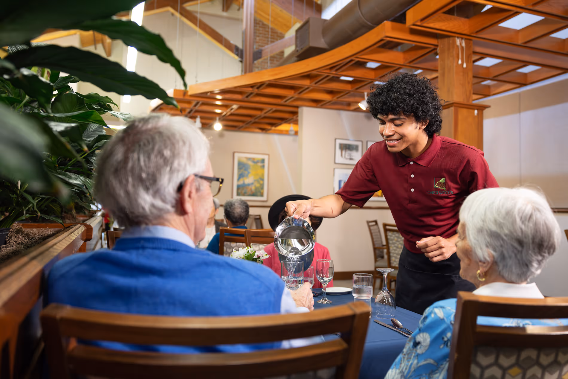 Waiter pours water for elderly couple sitting at a table in a restaurant.