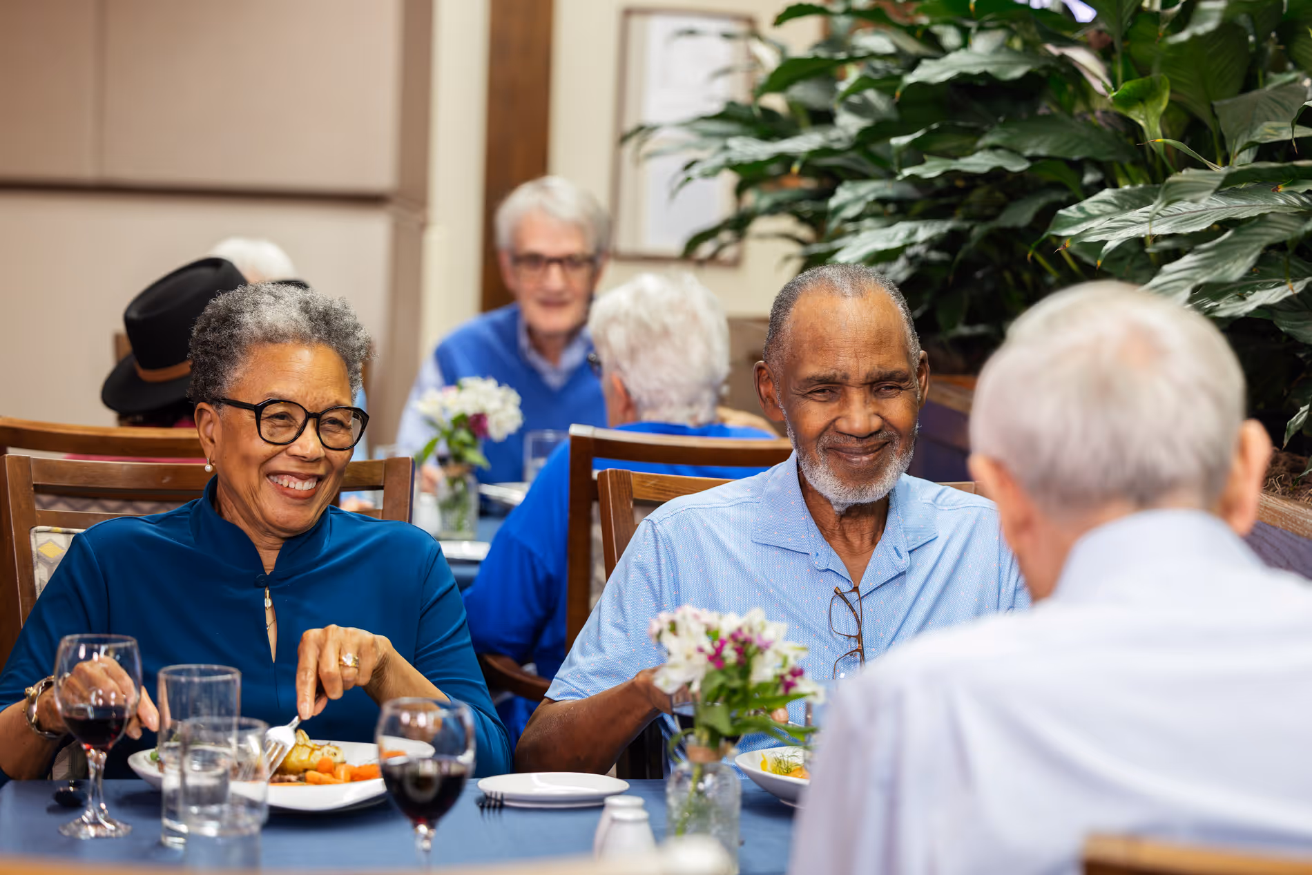 A group of older adults sit together, smiling and talking while dining at a restaurant.