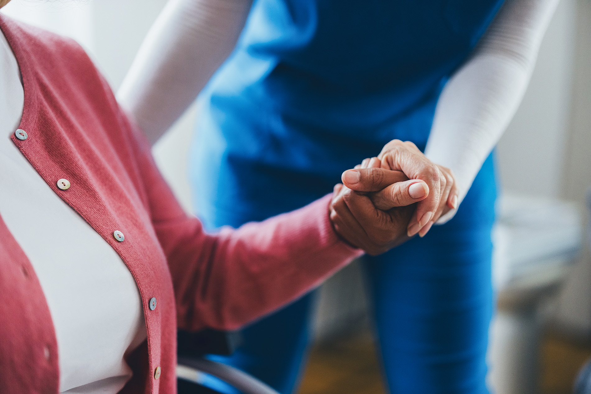 A caregiver gently holds an elderly person's hand, offering support and comfort.
