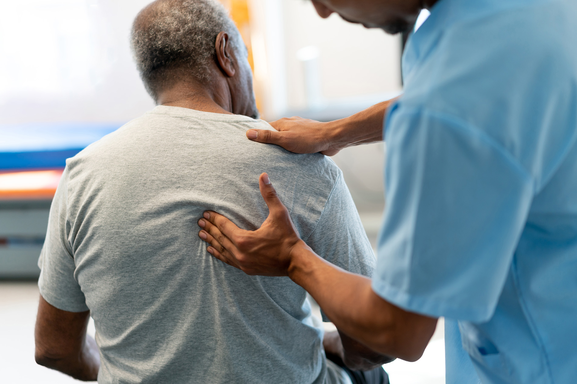A healthcare worker assists an elderly man by gently touching his back.