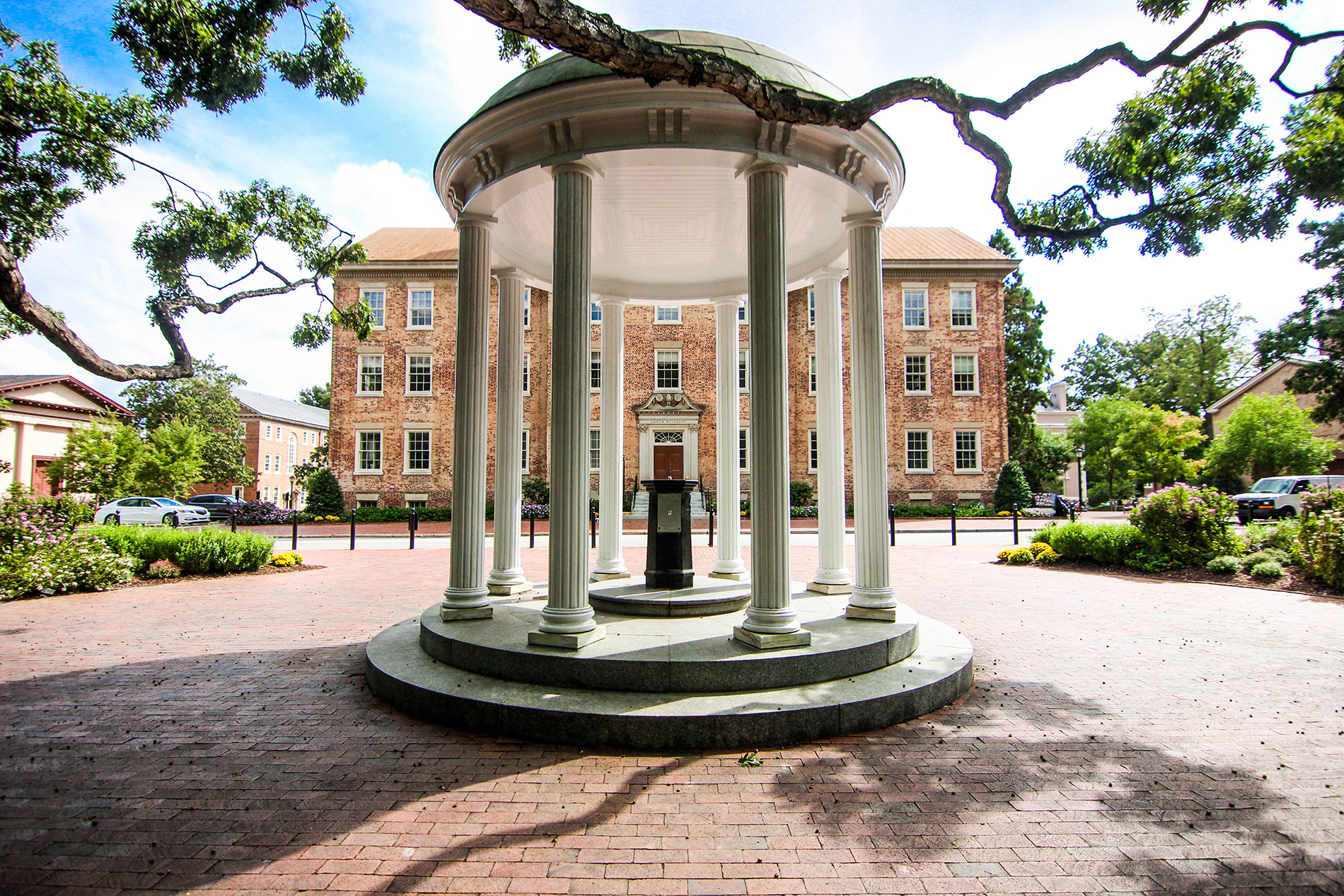 A white gazebo with tall columns stands in front of a large brick building.
