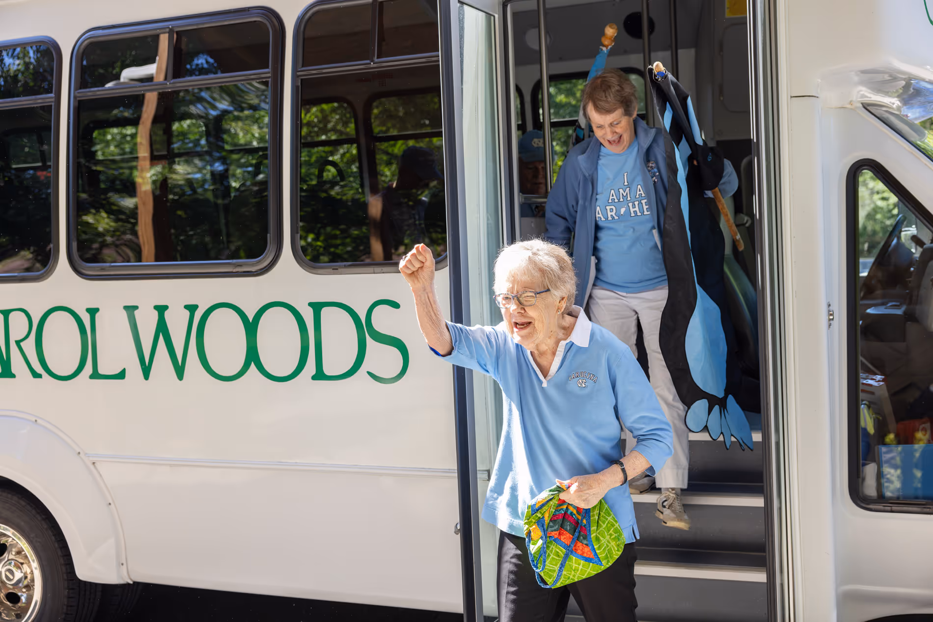 Elderly woman smiling and raising her fist triumphantly while exiting a bus with another woman.