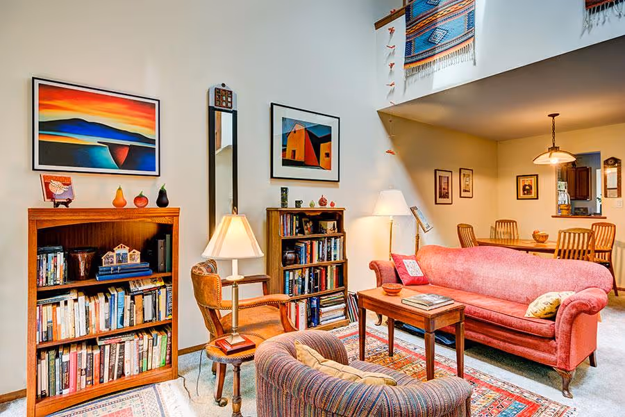A cozy living room with a red couch, bookshelves, and colorful wall art.