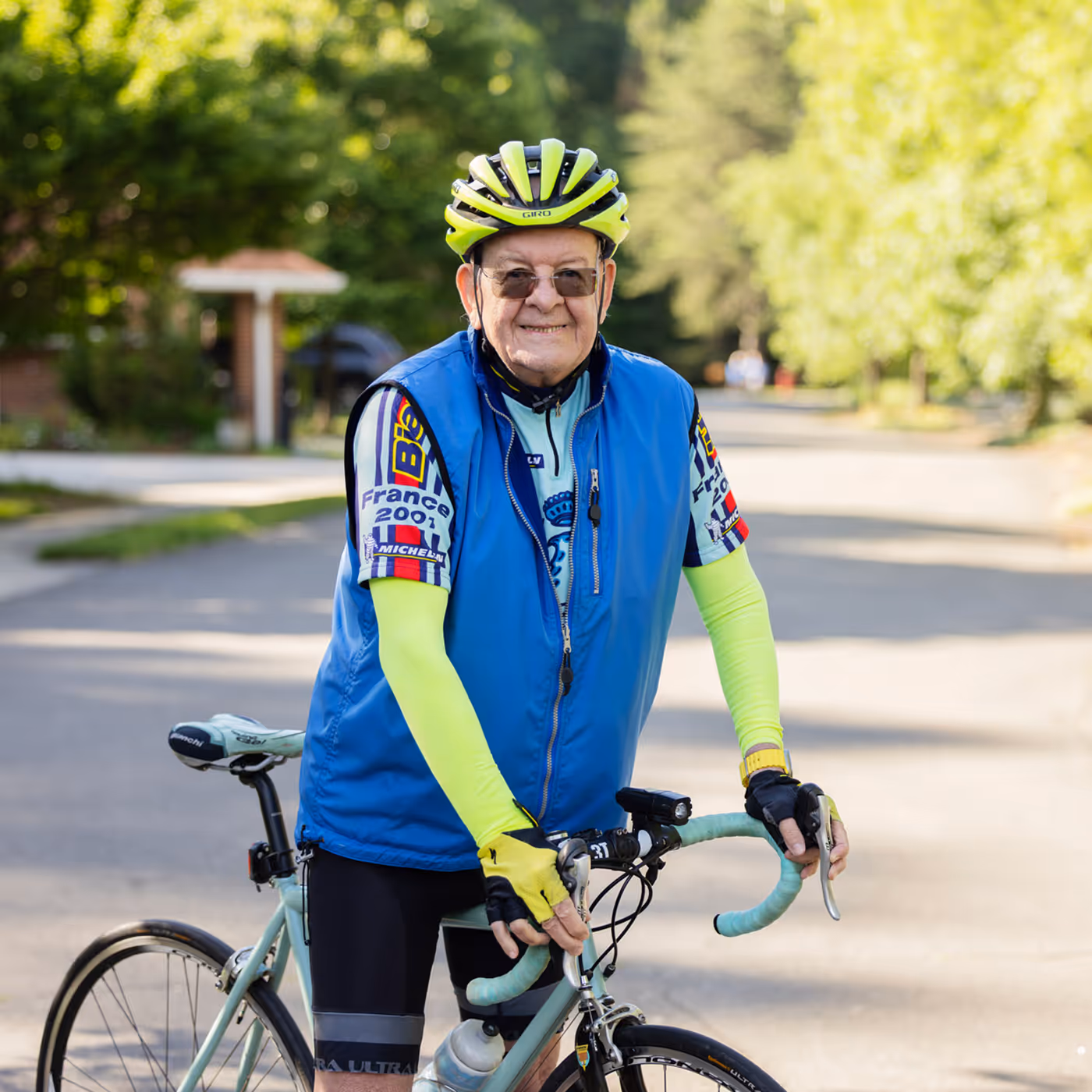 Elderly man in cycling gear poses with his bike on a sunny street.