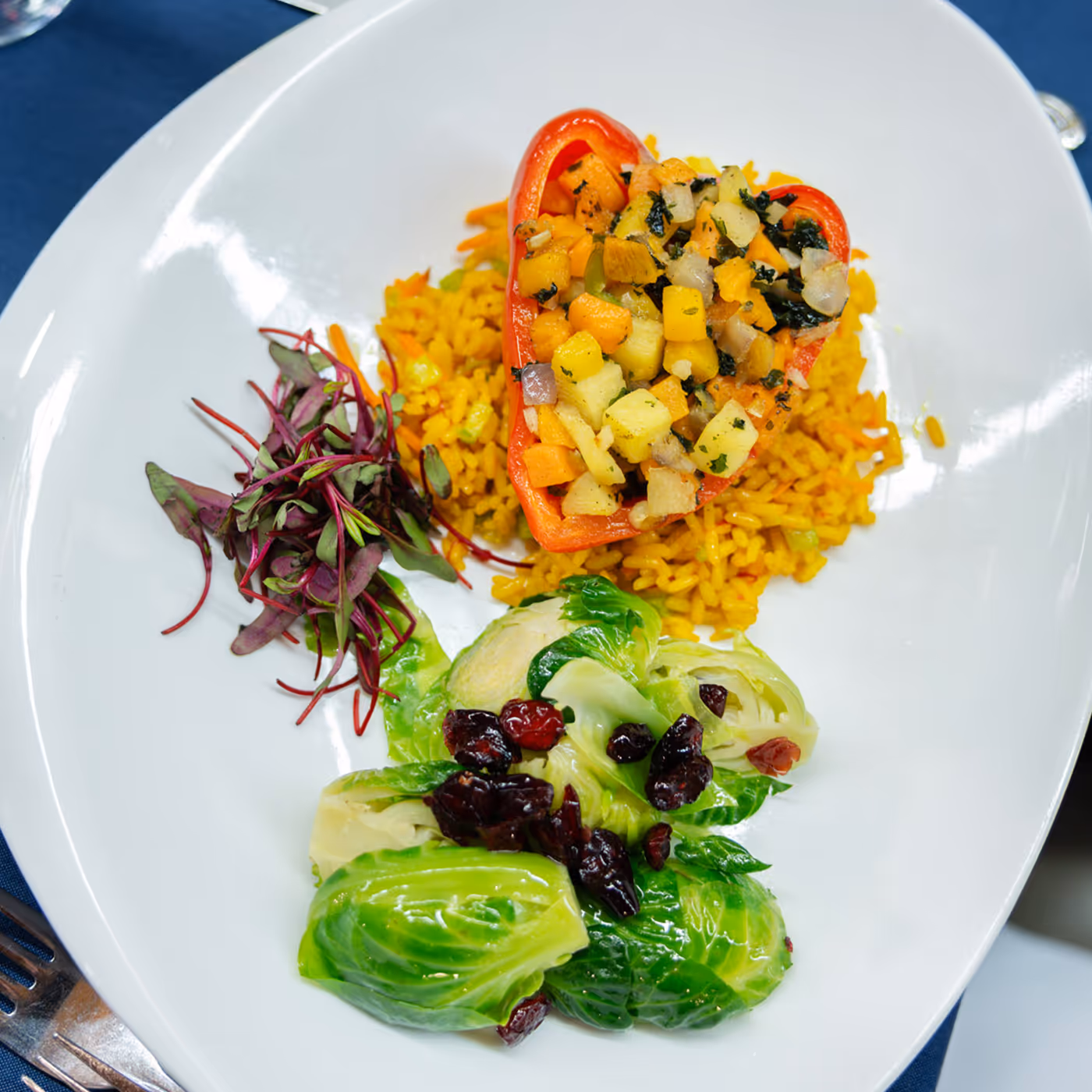 Stuffed red bell pepper on a white plate with yellow rice, Brussels sprouts, and microgreens.