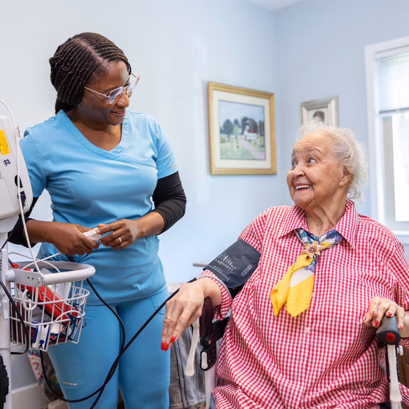 A nurse checks the blood pressure of a smiling elderly woman in a wheelchair.